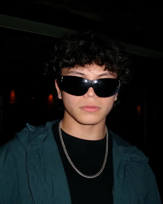 Dillon Lazo in dark wraparound sunglasses, a silver chain and a deep teal jacket